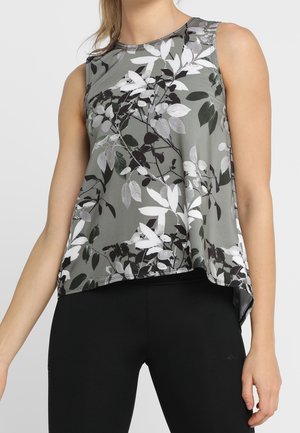 Mouwloos grijs topje met zwart-wit bladpatroon, gedragen met zwarte leggings, toont bovenlichaam en armen van persoon.