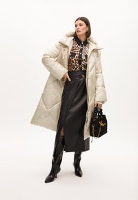 Vadderad beige jacka med huva, leopardmönstrad skjorta, svart läderkjol med sprund, svarta knähöga stövlar och en liten strukturerad svart väska.