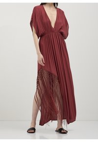 Red maxi dress with a deep V-neck, short sleeves, and a flowing silhouette. Features fringe detailing at the hem and lightweight fabric.