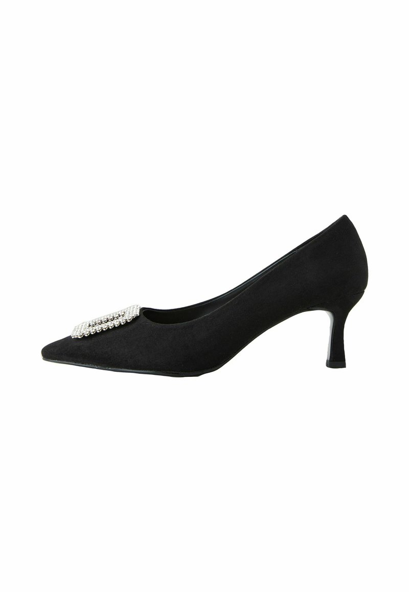 Escarpin en suède noir avec un bout pointu et un petit talon épais. Présente une boucle décorative avec des strass sur la partie des orteils.