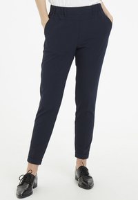 Pantalons fuselés bleu marine avec une taille plate, des poches latérales et des ourlets roulés, fabriqués en tissu léger et lisse.