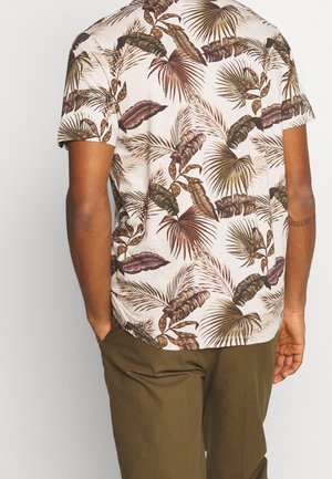 Short-sleeved shirt in light beige with green and brown tropical leaf patterns; relaxed fit, soft texture. Paired with olive green trousers.