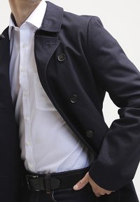 Sininen takki kaksirivisellä tyyliin, jossa on suuret napit, viistot kaulukset ja teksturoitu kangas. Puettuna valkoisen paidan päälle.