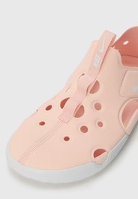 Pink Nike slip-on shoe with multiple ventilation holes, textured rubber sole, and a soft upper. Features a pull tab with branding.