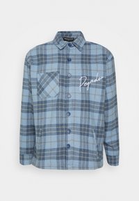 Camicia a quadri blu e grigia con colletto, tasca sul petto e scritta "Pegador" ricamata di bianco sul lato sinistro.