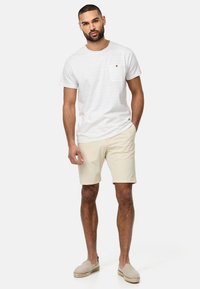 Weiß gestreiftes T-Shirt mit einer Brusttasche, kombiniert mit beigen Shorts und hellen Espadrilles. Lässiger, lockerer Schnitt; glatter Stoff.