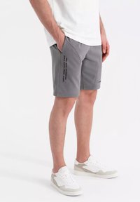 Shorts gris avec une coupe décontractée, dotés de poches latérales et d'un détail textuel sur la jambe gauche. Accompagnés de baskets blanches et grises.