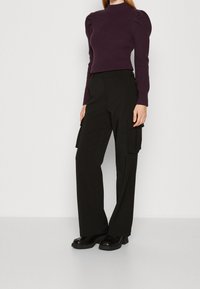 Fialový svetřík z žebrovaného úpletu s vysokým límcem a nafouklými rukávy, doplněný černými cargo kalhotami s postranními kapsami a rovného střihu.