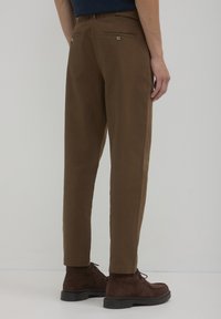 Chinos marroni con un design a gamba dritta, dotati di tasche posteriori con chiusura a bottone, abbinati a stivali in suede marrone scuro.