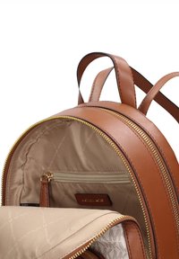 Sac à dos en cuir marron avec fermeture éclair dorée, poche intérieure zippée et doublure à motifs. Dispose de bretelles fines et d'une forme arrondie.