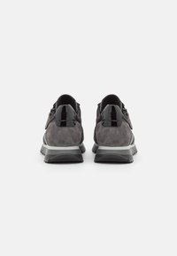 Graue Wildleder-Sneaker mit glänzenden schwarzen Akzenten, die eine strukturierte Oberfläche und eine kontrastierende weiße Zwischensohle aufweisen. Rückansicht, die die Designdetails zeigt.