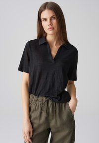 Polo shirt nero a maniche corte con scollatura a V, realizzato in un tessuto leggero. Abbinato a pantaloni verdi oliva dal taglio comodo con vita elastica.