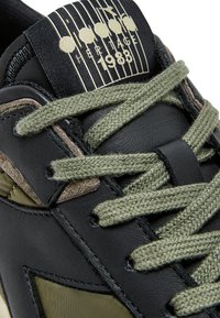 Sneaker in pelle nera con accenti verde oliva, lacci testurizzati e un'etichetta a linguetta con motivo che recita "Heritage 1988".