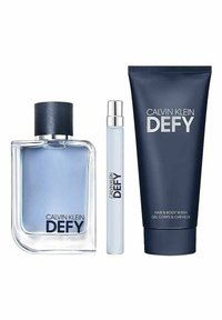 Calvin Klein Defy tuoksusarja: lasipullo, jossa on sinistä nestettä ja tumma korkki, rullapullo sekä tummansininen putki hius- ja vartalopesua varten, kaikki merkitty.