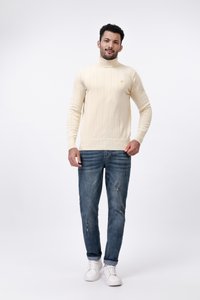 Beige bordázott garbó pulóver hosszú ujjakkal, vékony szabású, koptatott kék farmernadrággal és fehér sportcipőkkel párosítva.