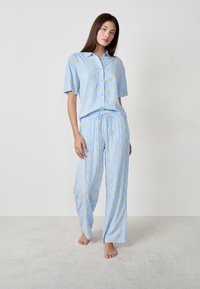 Set di pigiama azzurro chiaro con motivo di anatre gialle. Camicia con maniche corte e bottoni, e pantaloni a righe larghi con cintura elastica.