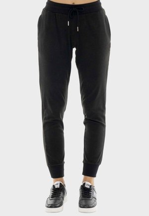 Pantaloni jogger neri affusolati con vita con coulisse e polsini elastici, indossati con sneakers nere e bianche su una persona in piedi.