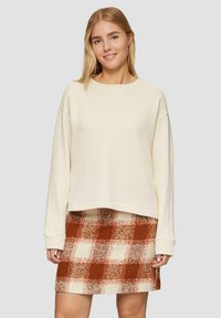 Crème cropped sweatshirt met verlaagde schouders, gecombineerd met een rood-wit geruite rok, met een gestructureerde stof en zichtbare naden.