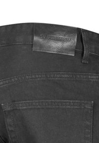 Jeans de denim negro con una etiqueta de cuero que dice "Zy Premium." Las características incluyen bolsillos cosidos y una textura suave y resistente.