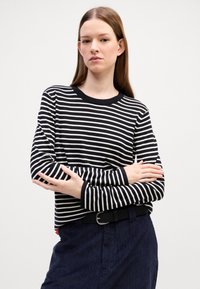 Svart og hvit stripete langermet topp med rund hals, kombinert med marineblå kordfløyelsbukser og et svart belte.