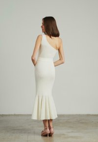 Weißes, geripptes Ein-Shoulder-Kleid mit taillierter Oberseite, ausgestellt am Saum und mit einem strukturierten Muster. Kombiniert mit rosafarbenen Absätzen.