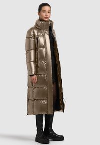 Metallic gold puffer coat with a high collar, zippered closure, and rectangular quilted patterns. Worn over a black outfit and knee-high boots.
