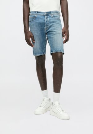 Shorts in denim azzurro chiaro con un design classico, caratterizzati da una vita media, cinque tasche e orli arrotolati, abbinati a sneaker bianche.