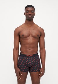 Svarta boxershorts med en röd "Levi's"-logotyp och ett upprepande textmönster. Tyget verkar slätt och åtsittande, med en mjuk midjeresår.