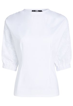 Biała bluzka z krótkim rękawem, z bufkami z haftowanej koronki z dziurkami i subtelnym haftowanym logo na piersi.