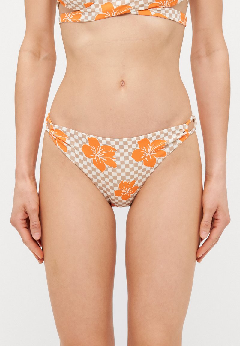 Bas de bikini avec un motif floral beige et orange sur un fond à carreaux, des détails de ruching sur les côtés et une coupe taille basse.