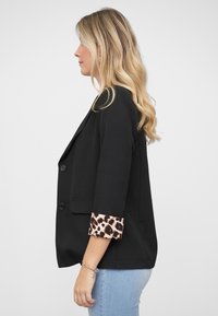 Svart blazer med skreddersydd passform, med leopardmønsterdetaljer på mansjetten. Dobbel knappelukking og trekvartlange ermer.