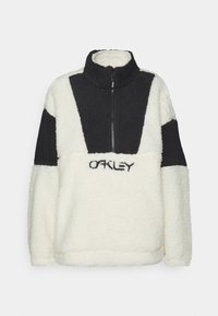 Fleece-Pullover in Creme und Schwarz, mit hohem Kragen, Reißverschluss vorne und kontrastierendem Paneldesign. "OAKLEY"-Logo in schwarzem Stick.