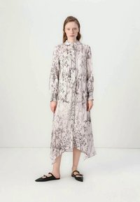Vestido longo, de flores em rosa claro, com fecho de botões na parte da frente, cintura franzida e barra assimétrica. Acentuado por mangas bufantes longas e um delicado padrão em preto.