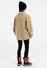 Veste oversize en polaire beige avec un col, leggings noirs et bottes en cuir imperméables marron avec doublure en fourrure et lacets rouges.