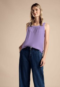 Lila ärmelloses Oberteil mit gerafftem Ausschnitt, kombiniert mit lockeren dunklen Jeans. Das Oberteil hat eine glatte Textur und einen lässigen Schnitt.