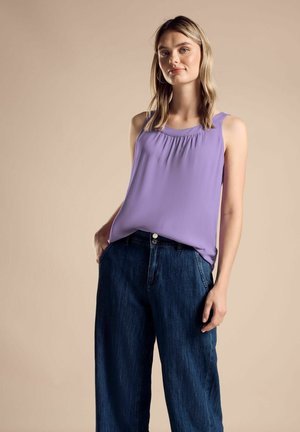 Top viola senza maniche con scollo arricciato, abbinato a jeans scuri in denim larghi. Il top ha una superficie liscia e una vestibilità rilassata.