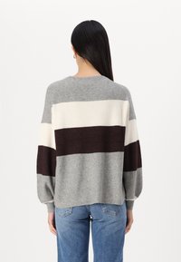 Pull rayé gris et crème avec une coupe décontractée, texture côtelée, col rond et manches ballons, associé à un jean bleu clair.