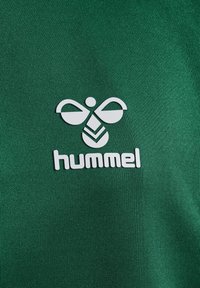 Grønn skjorte med teksturert stoff og hvitt Hummel-logo med et stilisert bie-design over merkenavnet.