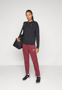 Sudadera negra, pantalones de chándal burdeos con logo y zapatillas deportivas negras. Sosteniendo un bolso de deporte negro. Diseño sencillo y casual de ropa deportiva.