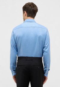 Camicia azzurra a maniche lunghe con colletto button-down, texture liscia, e pantaloni neri con due tasche posteriori e bottoni.