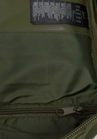 Olivegrön zippered väska inuti, med en slät, texturerad polyestertyg. Inkluderar svart skötselmärke med skötselinstruktioner.
