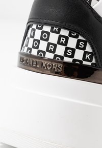 Baskets en cuir noir avec un motif à carreaux blanc et noir, des détails en bronze et une semelle épaisse blanche embossée du logo "MICHAEL KORS".