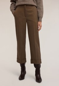 Bruna vida byxor med vid ben och ankellånga bruna läderstövlar i mörkbrun färg, kombinerat med en strukturstickad brun tröja.