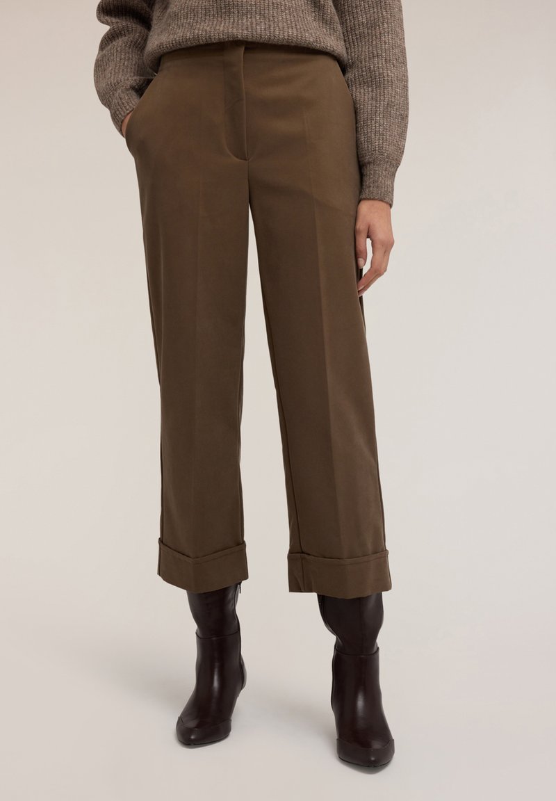 Bruna vida byxor med vid ben och ankellånga bruna läderstövlar i mörkbrun färg, kombinerat med en strukturstickad brun tröja.