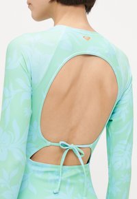 Long-sleeve swimsuit in light mint green with floral pattern. Features a scoop back with ties for adjustment. Smooth, stretchy fabric.