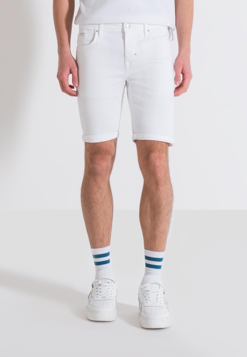 Shorts de mezclilla blanca con puños doblados, que presentan un diseño clásico de cinco bolsillos y costuras resistentes, combinados con zapatillas blancas y calcetas a rayas.