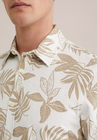 Short-sleeve shirt made of light fabric featuring a cream base with a tan leaf pattern, pointed collar, and button closure details.