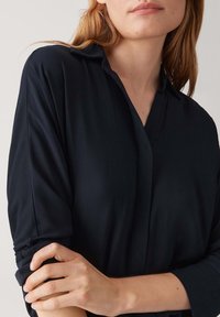 Blusa nera a maniche lunghe con colletto e maniche a risvolto, caratterizzata da una texture liscia e una vestibilità rilassata per il massimo comfort.