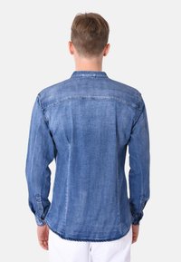 Camicia in denim azzurro chiaro con bottoni, dotata di maniche lunghe, colletto classico e dettagli di cucitura lungo la schiena e le spalle.