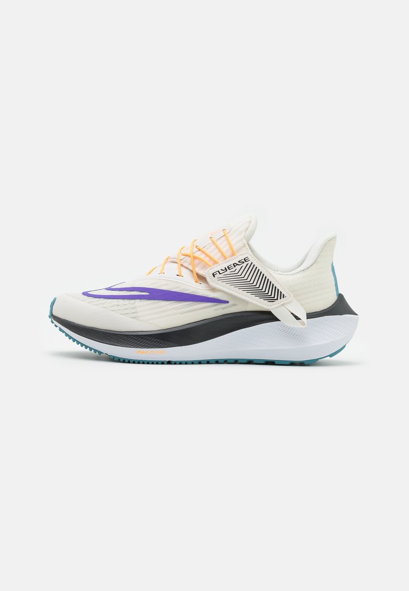Chaussure de sport blanche avec virgule violette, lacets orange, semelle noire et blanche, et une bride "Flyease" pour une fermeture facile.